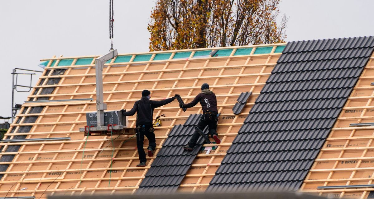 Deux couvreurs posent des tuiles sur le toit d'une maison
