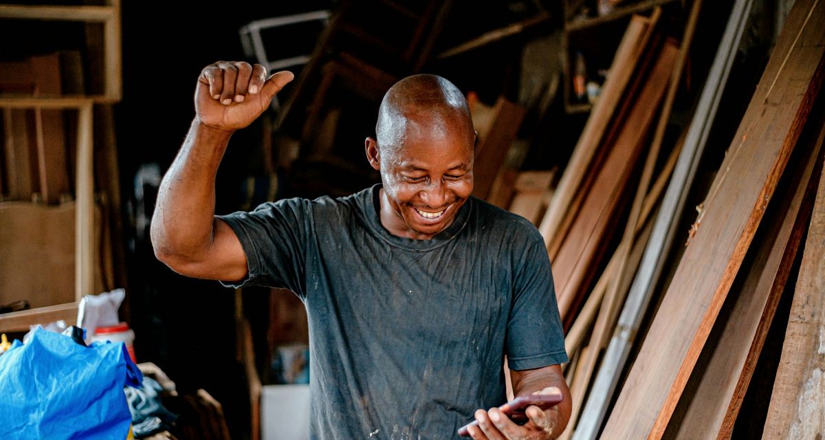 Un artisan dans son atelier se réjouit en regardant son téléphone